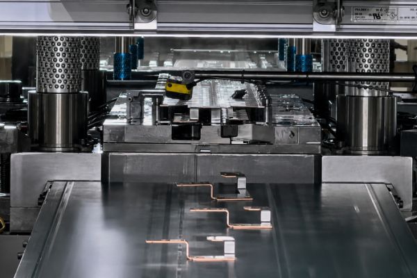 Die stamping press producing small metal terminals for UAV components on a conveyor.